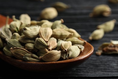 Spoon with dry cardamom pods on black wooden table, closeup