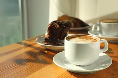 Photo of Cup of fresh aromatic coffee and cupcake at table in cafe