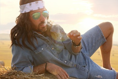 Photo of Hippie man smoking joint on hay bale in field