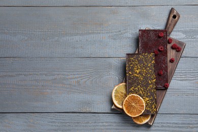 Photo of Board and different chocolate bars with freeze dried fruits on grey wooden table, top view. Space for text