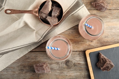 Photo of Flat lay composition with jars of tasty chocolate milk on wooden background. Dairy drink