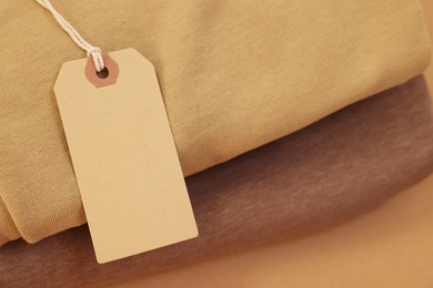 Photo of Garment with cardboard tag on beige background, closeup. Space for text