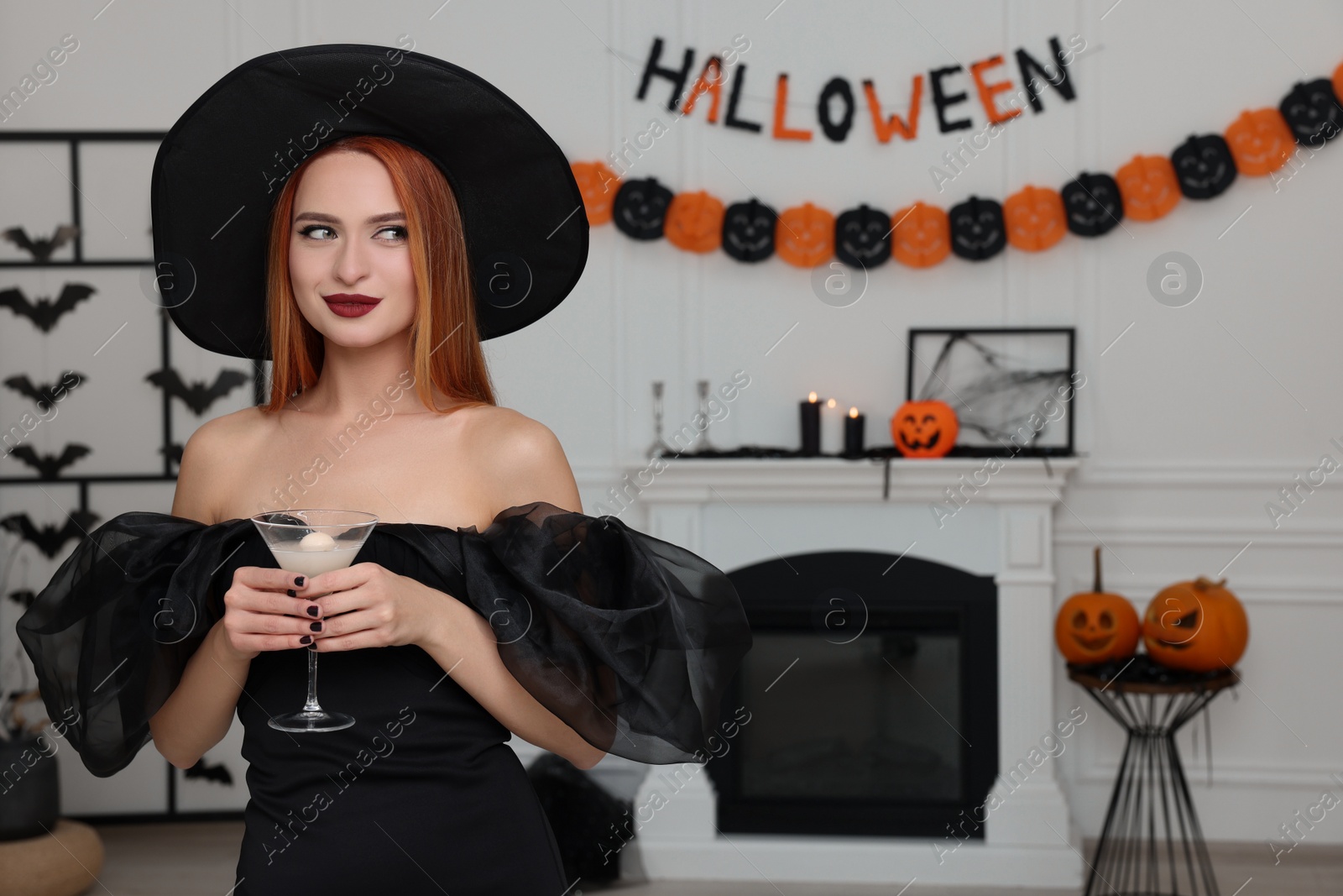 Photo of Young woman in scary witch costume with glass of cocktail indoors, space for text. Halloween celebration