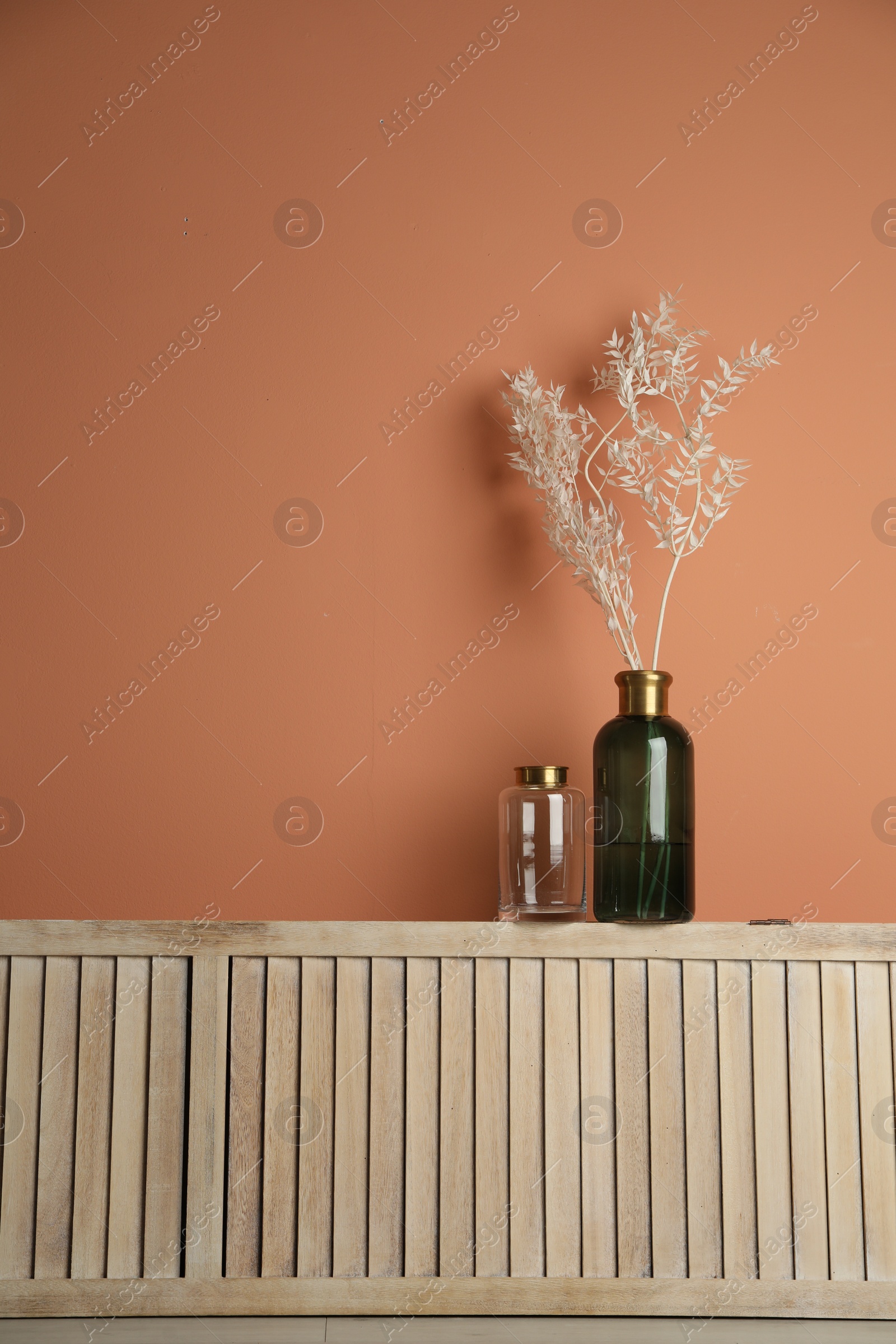 Photo of Decorative vases on wooden shelf near wall indoors