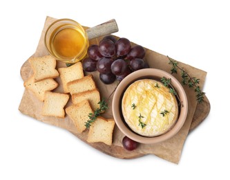 Tasty baked camembert in bowl, croutons, grapes, honey and thyme on white background, top view