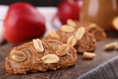 Photo of Pieces of fresh apple with peanut butter on wooden board, closeup