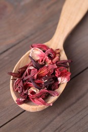 Photo of Spoon of dry hibiscus tea on wooden table, closeup