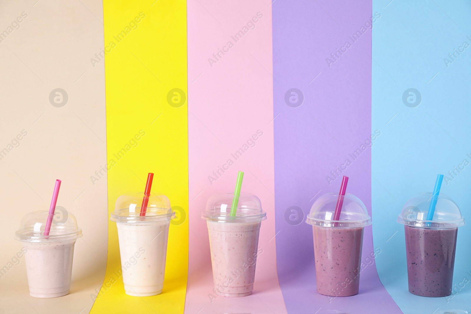 Photo of Different tasty milk shakes in plastic cups on color background. Space for text