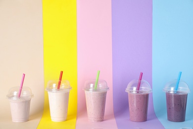 Photo of Different tasty milk shakes in plastic cups on color background. Space for text