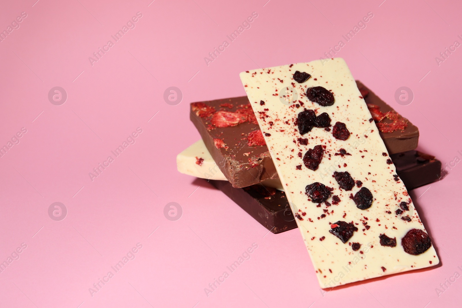 Photo of Different chocolate bars with freeze dried fruits on pink background, space for text