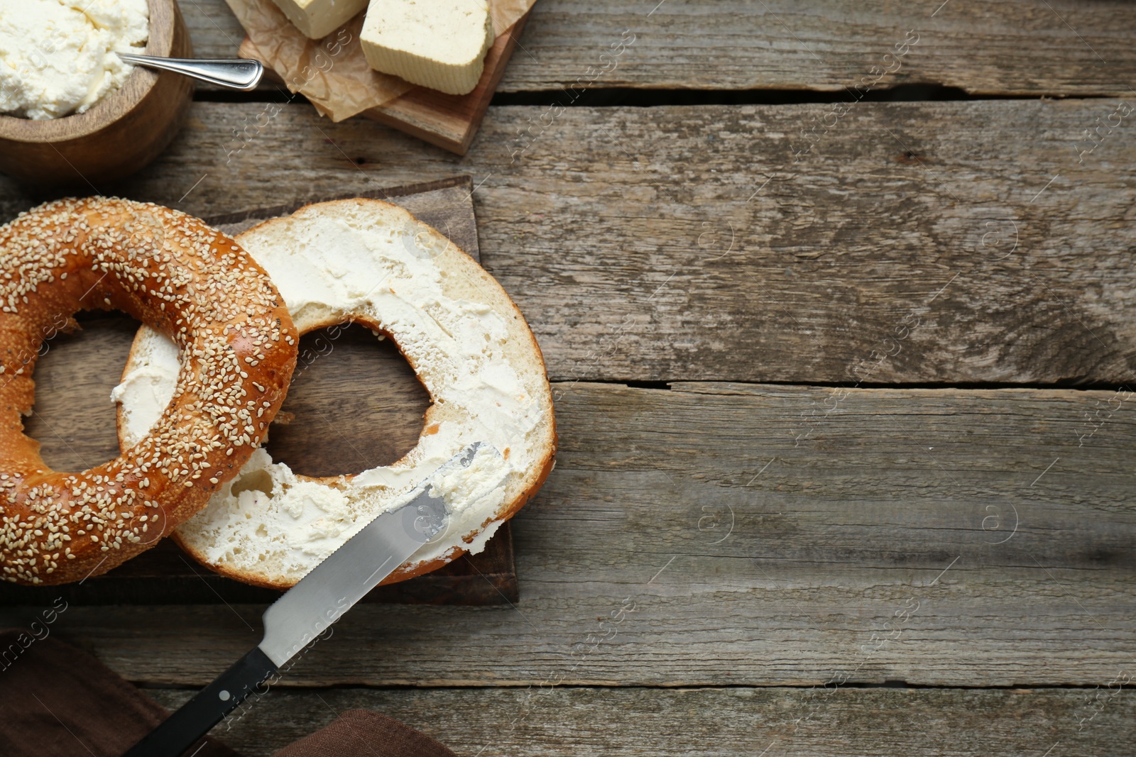 Photo of Delicious bagel with tofu cream cheese and knife on wooden table, flat lay. Space for text