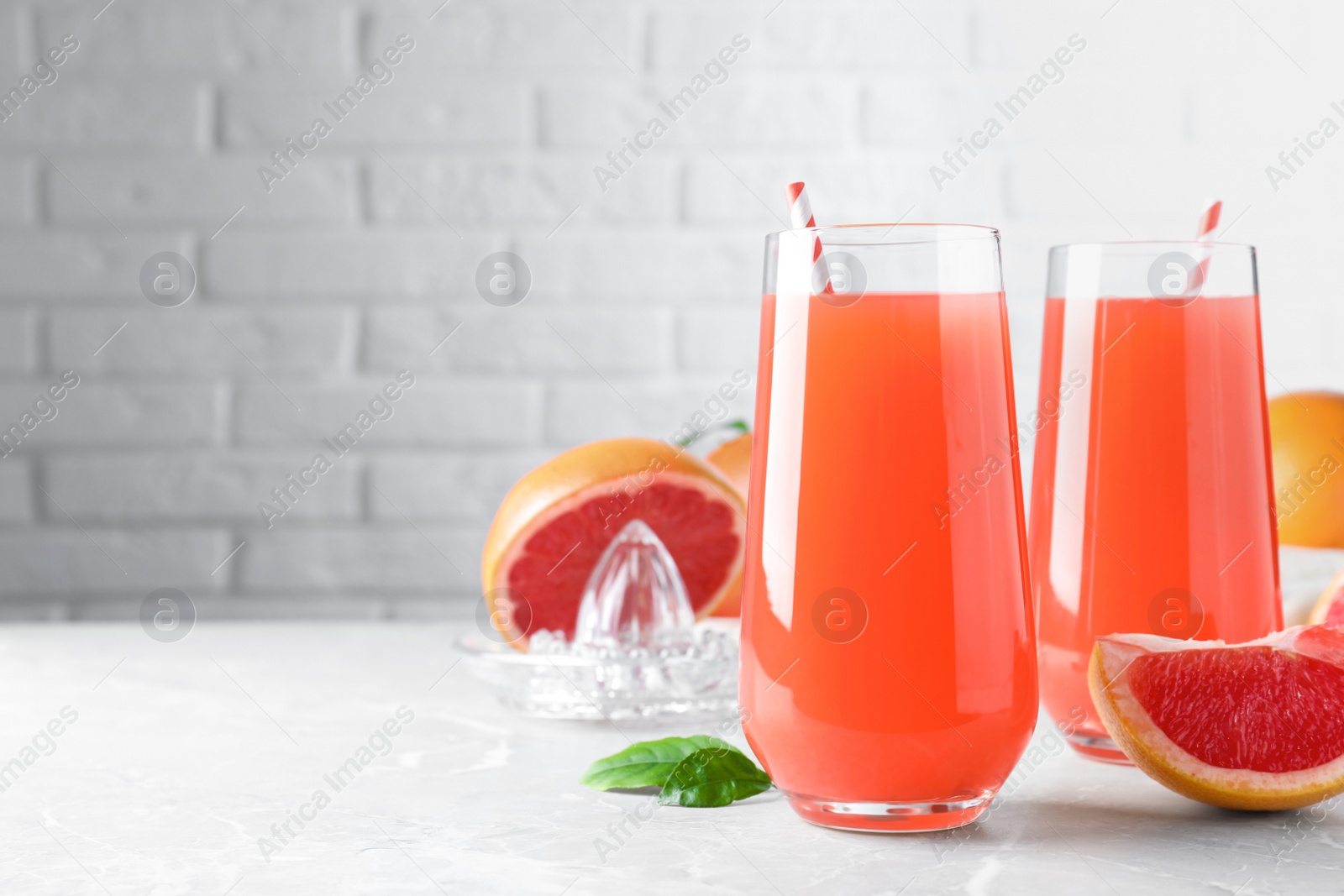 Photo of Tasty freshly made grapefruit juice and fruit on light grey marble table. Space for text