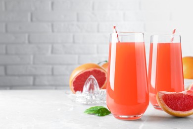 Photo of Tasty freshly made grapefruit juice and fruit on light grey marble table. Space for text