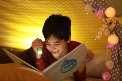 Photo of Boy with flashlight reading book in play tent at home