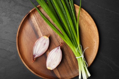 Photo of Bunch of fresh green onion and halved bulb on black table, top view