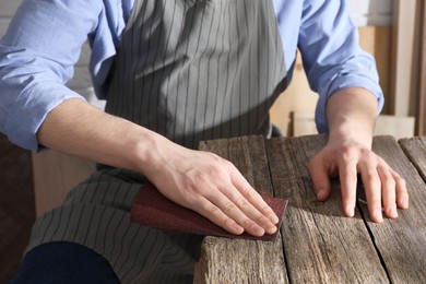 Man polishing wooden table with sandpaper indoors, closeup