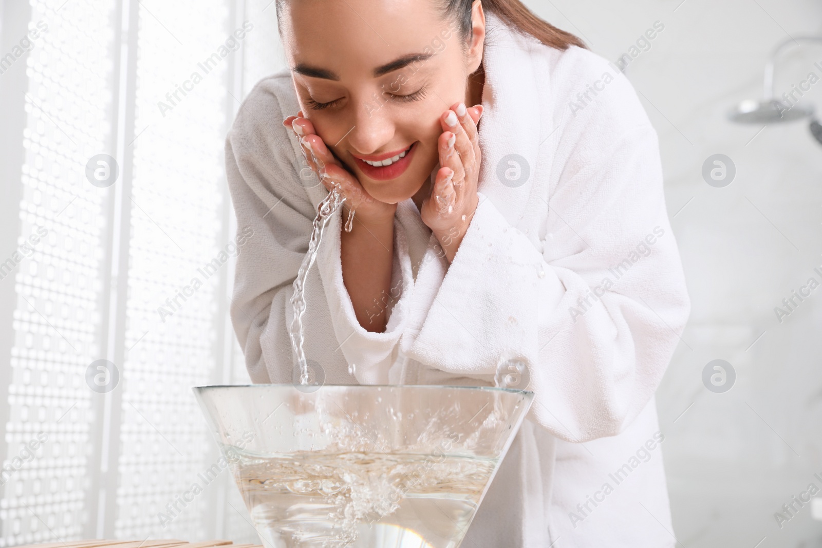 Photo of Beautiful young woman washing her face with water in bathroom