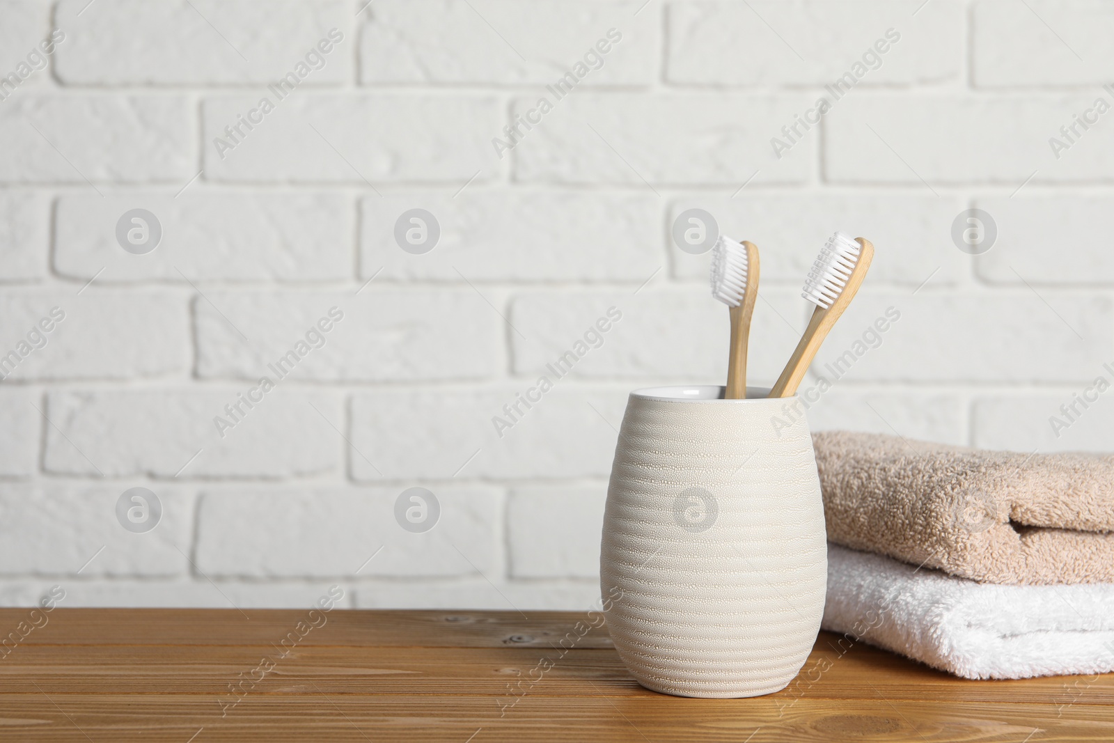 Photo of Bamboo toothbrushes in holder and towels on wooden table. Space for text