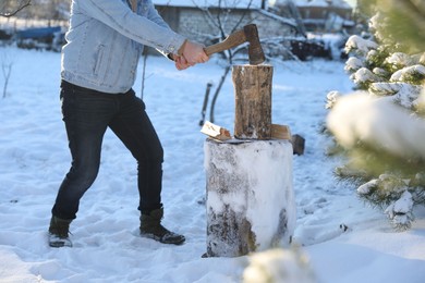 Photo of Man chopping wood with axe outdoors on winter day, closeup