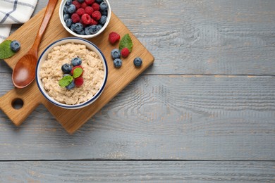 Photo of Tasty oatmeal porridge with berries on grey wooden table, top view. Space for text