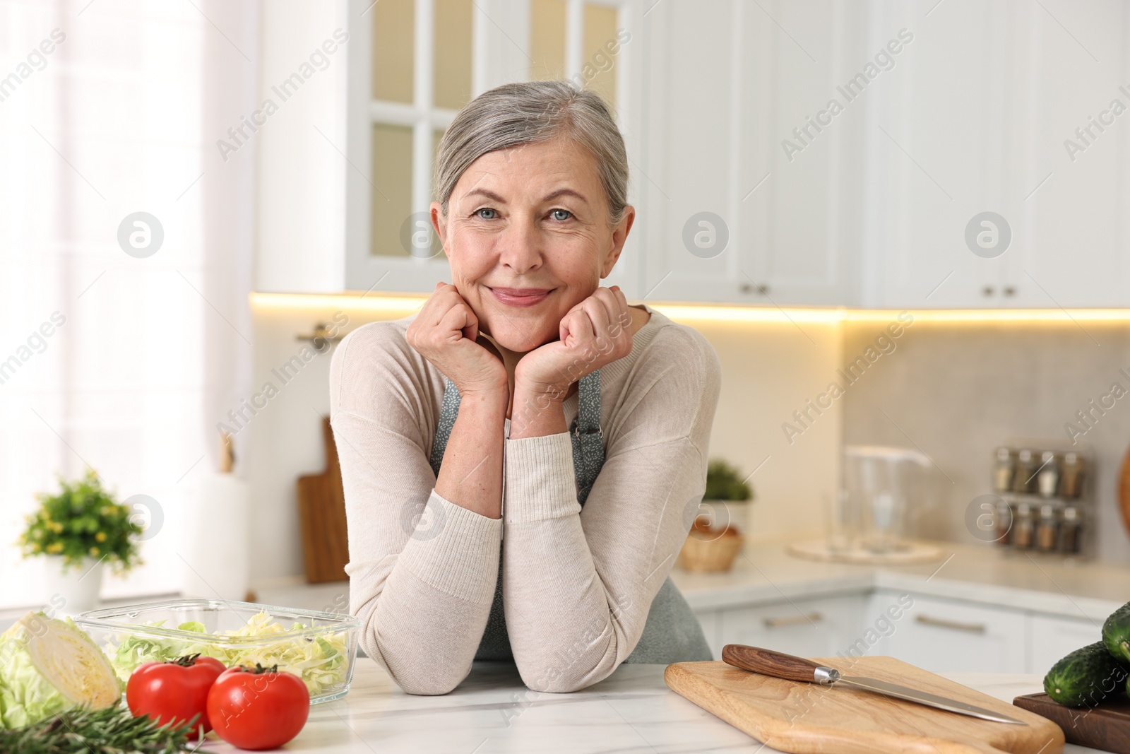 Photo of Happy housewife at white table in kitchen. Cooking process