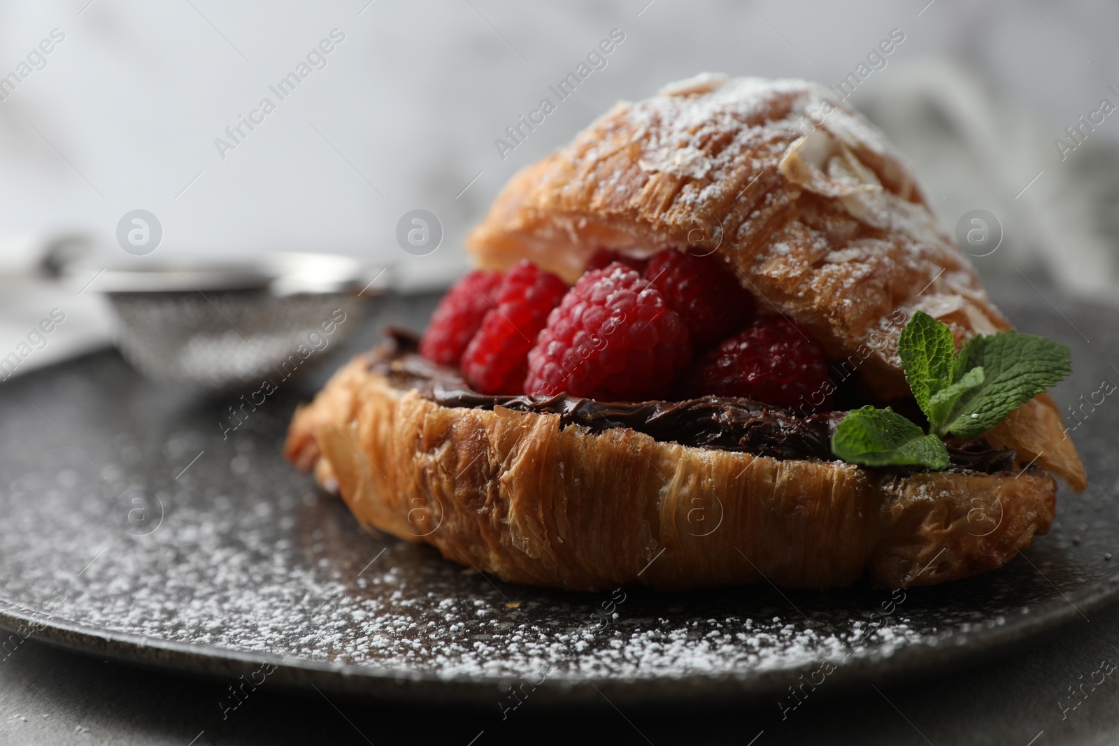 Photo of Delicious croissant with raspberries, chocolate and powdered sugar on table, closeup. Space for text
