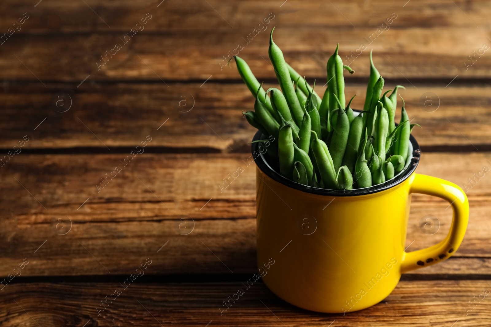 Photo of Fresh green beans in mug on wooden table, space for text