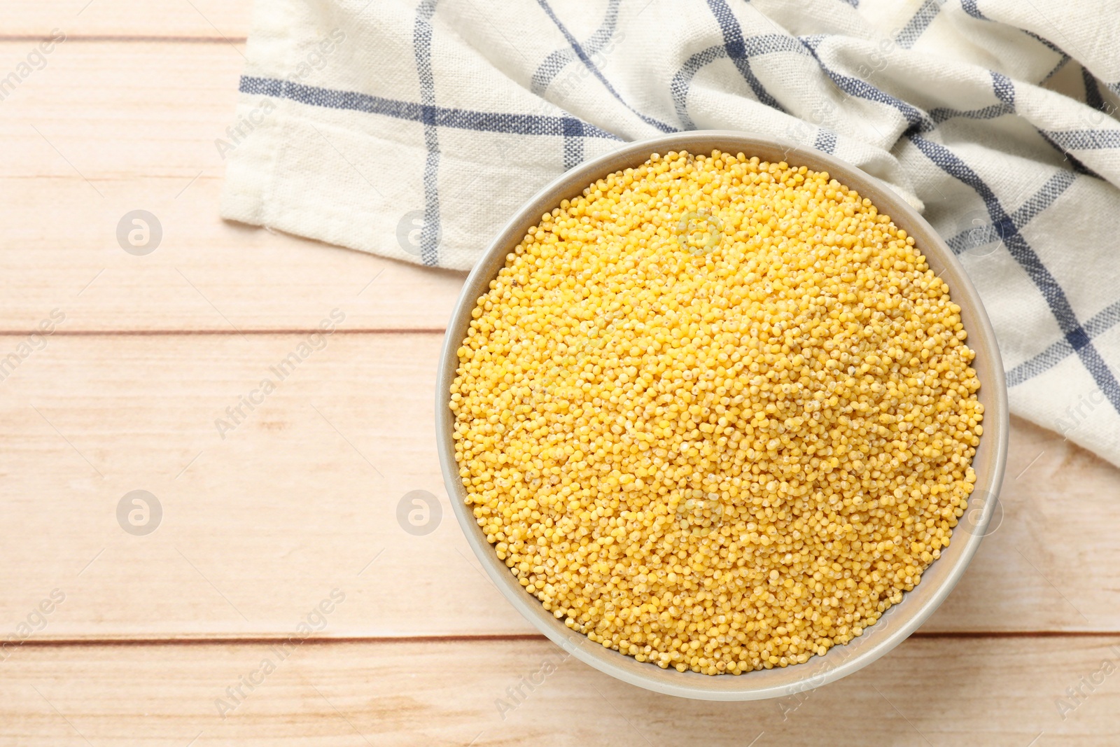 Photo of Millet groats in bowl on light wooden table, top view. Space for text