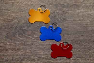 Color metal pet tags in shape of bones with ring on wooden table, flat lay. Space for text