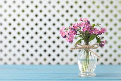 Beautiful pink forget-me-not flowers in glass bottle on light blue wooden table. Space for text