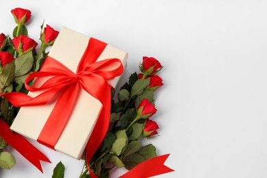 Beautiful gift box with bow and red roses on white background, flat lay. Space for text