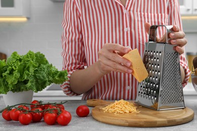 Photo of Woman grating cheese at kitchen table, closeup