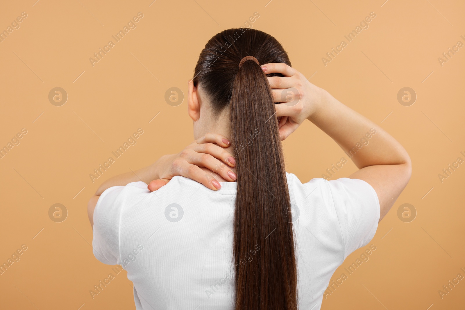 Photo of Woman touching her neck and head on beige background, back view