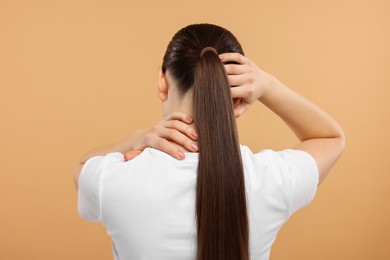 Photo of Woman touching her neck and head on beige background, back view