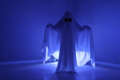 Photo of Creepy ghost. Woman covered with sheet in blue light