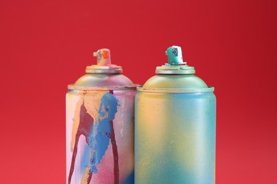 Photo of Two spray paint cans on red background, closeup