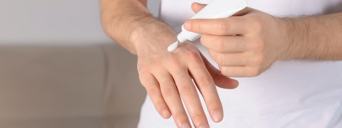 Image of Man applying cream onto hand at home, closeup. Banner design