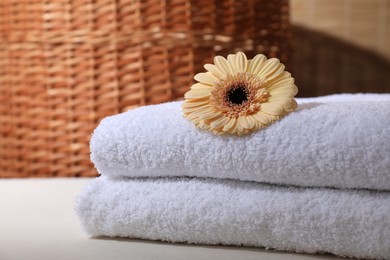 Photo of Stacked terry towels and flower on white table indoors, closeup. Space for text