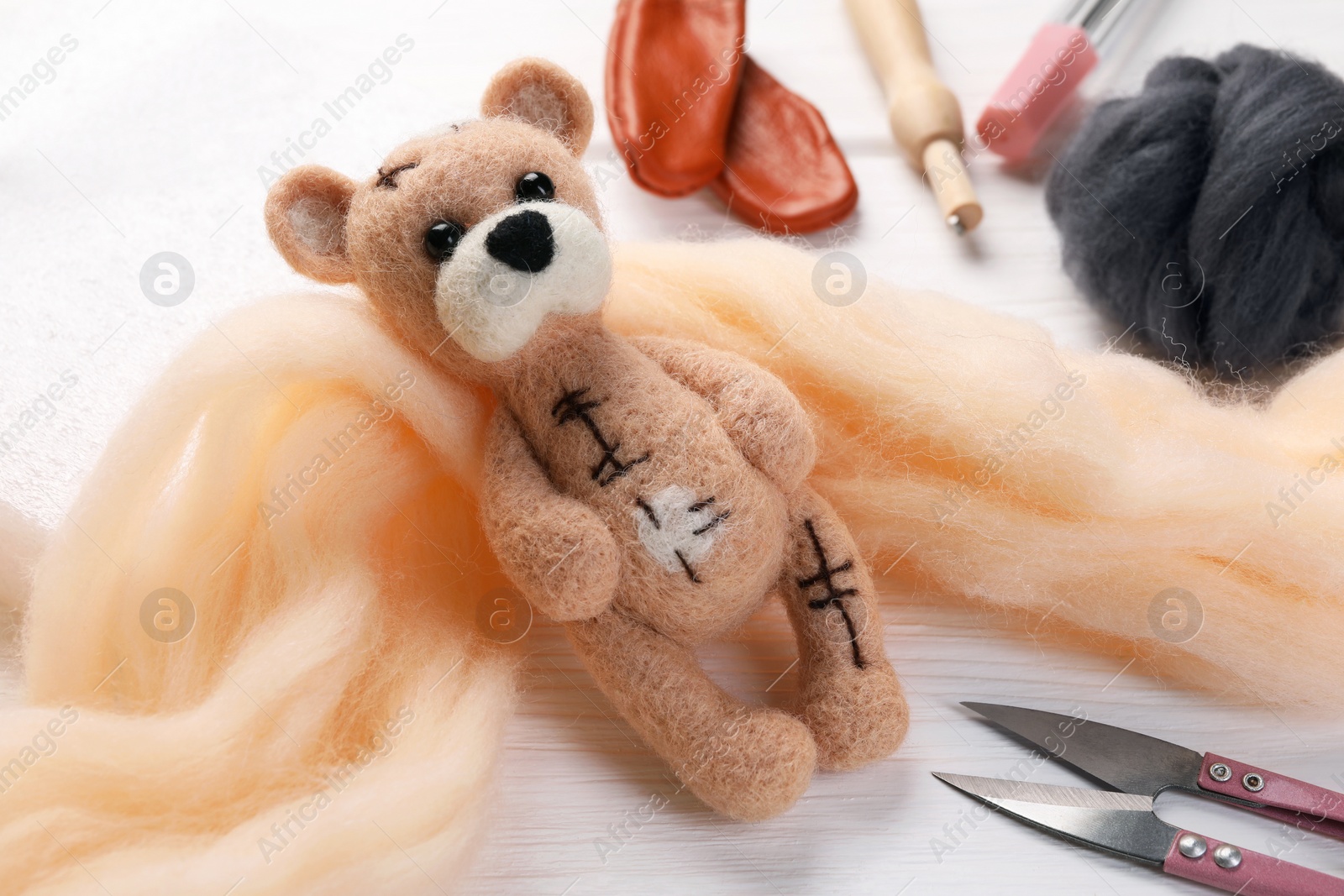 Photo of Felted bear, wool and tools on white wooden table, closeup