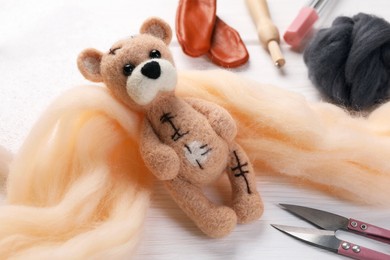 Photo of Felted bear, wool and tools on white wooden table, closeup