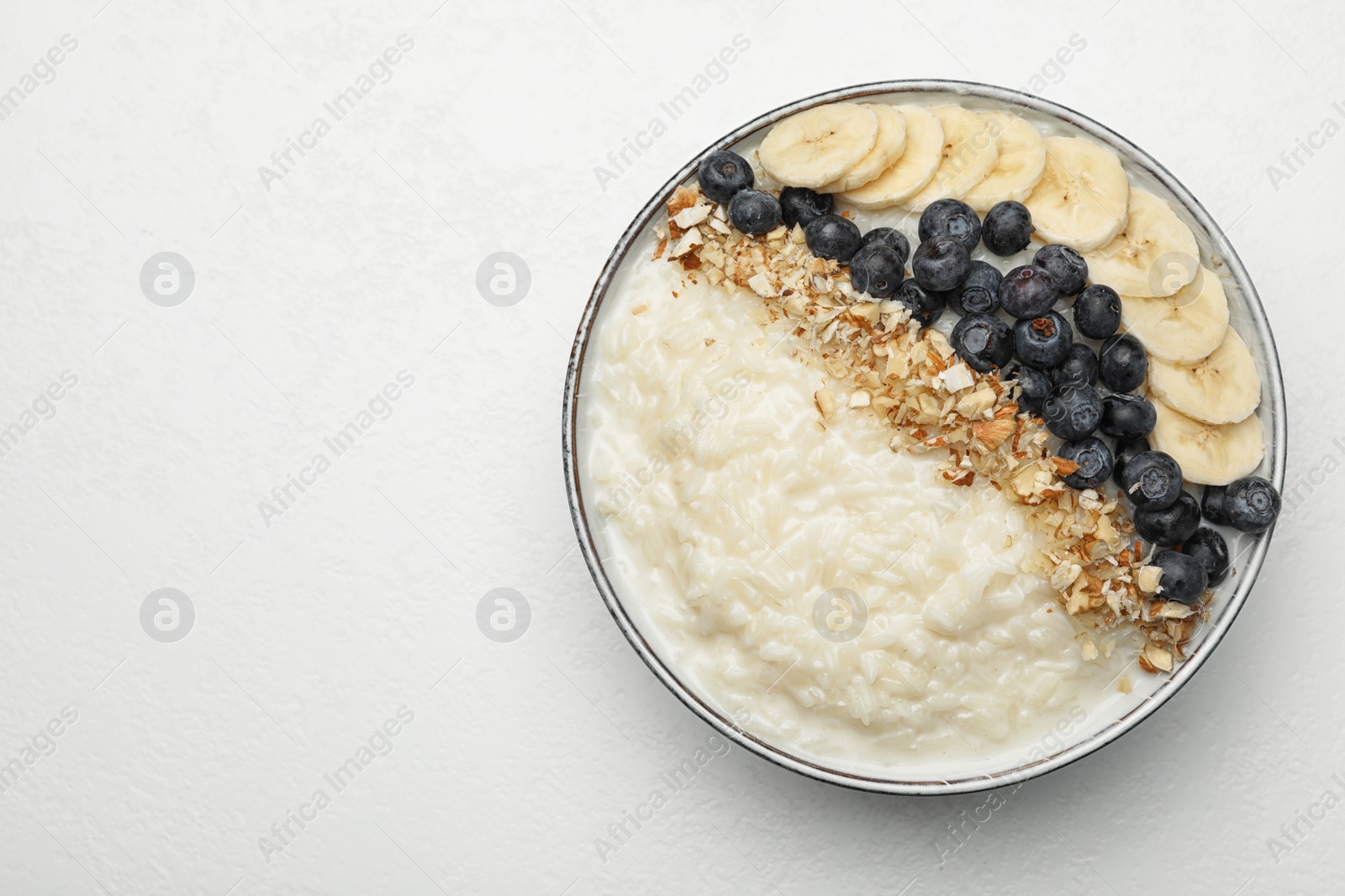 Photo of Delicious rice pudding with banana, blueberries and almond on light table, top view. Space for text