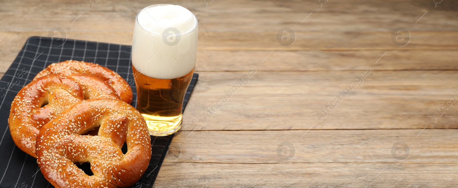 Image of Tasty pretzels and glass of beer on wooden table, space for text. Banner design