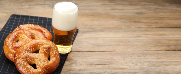 Image of Tasty pretzels and glass of beer on wooden table, space for text. Banner design