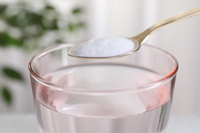 Spoon with baking soda over glass of water on blurred background, closeup