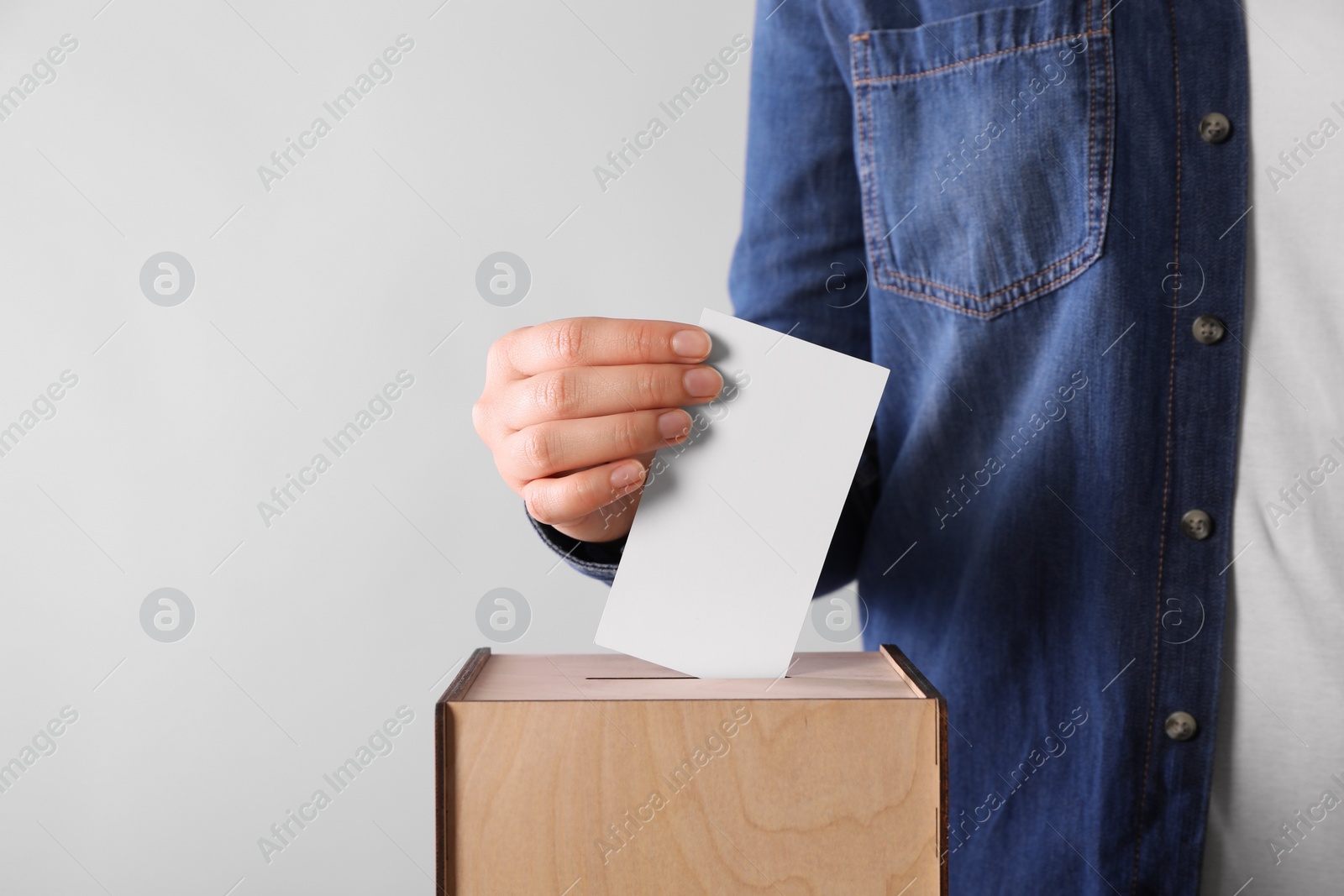 Photo of Woman putting her vote into ballot box on light grey background, closeup. Space for text