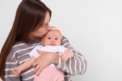 Photo of Mother kissing her cute baby on light background, space for text