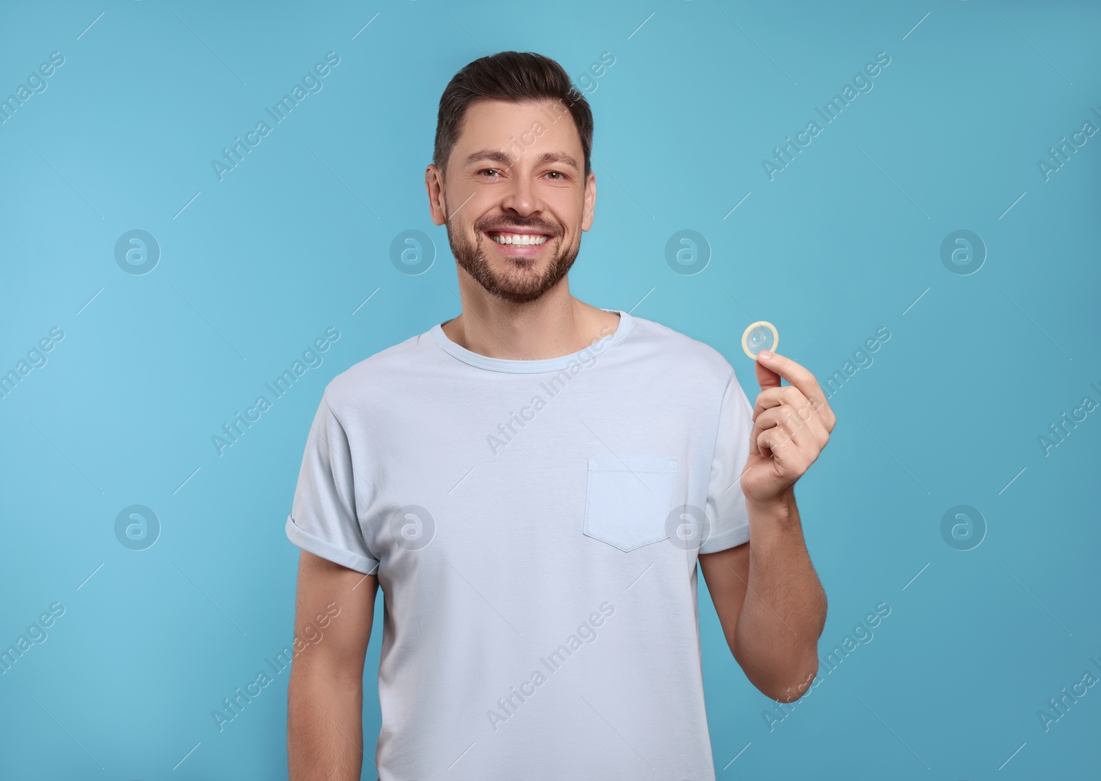 Photo of Happy man holding condom on light blue background