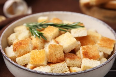 Photo of Delicious crispy croutons with rosemary in bowl, closeup