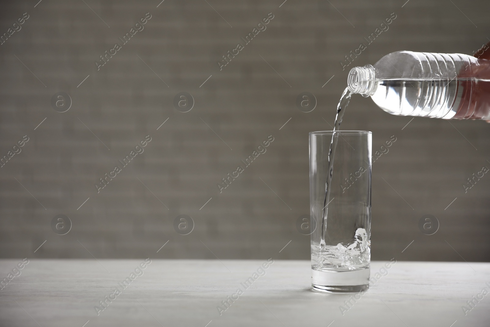 Photo of Pouring water from bottle into glass on table against blurred background. Space for text