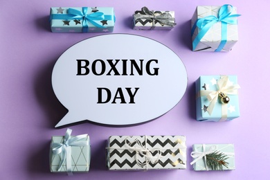 Speech bubble with phrase BOXING DAY and Christmas decorations on lilac background, flat lay